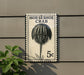 A postage stamp featuring a horseshoe crab, mounted on a wall next to a plant.