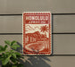 A red and white sign with the text "HONOLULU, HAWAII USA" and an illustration of a beach and palm trees, mounted on a wall next to a plant.