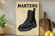 a wooden sign with a black and white illustration of a black boot, placed on a wooden surface next to a wooden cutting board and a potted plant.