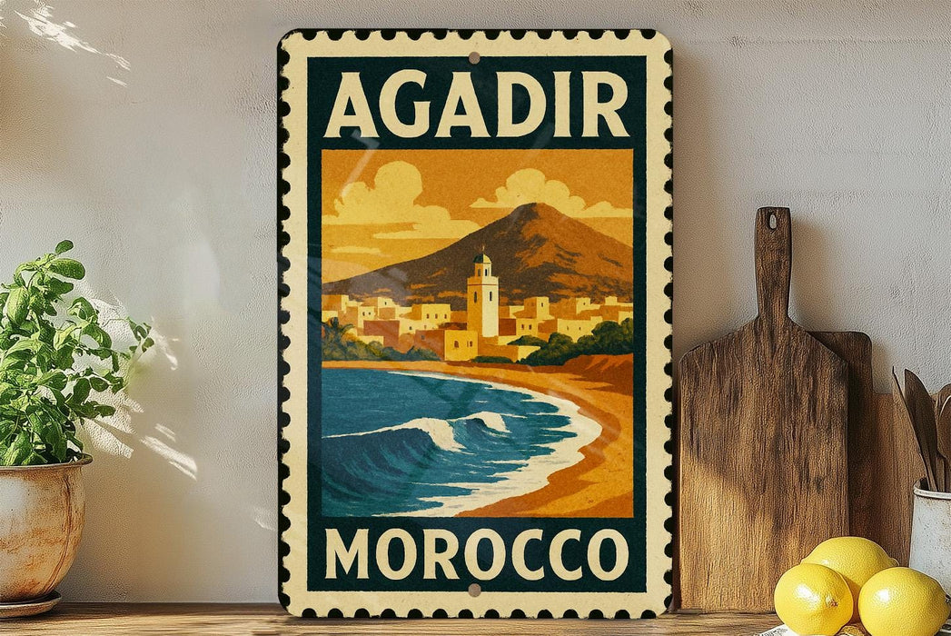 A vintage-style metal stamp with the text "AGADIR MOROCCO" and an illustration of a coastal city with mountains in the background.