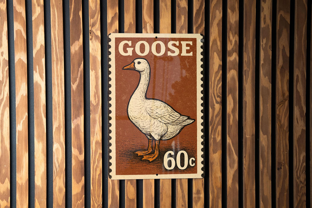 A postage stamp featuring a white goose with orange feet is displayed on a wooden wall.