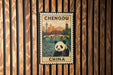 A poster of a panda bear and the city of Chengdu, China, displayed on a wooden wall.