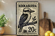 A metal sign with a black and white illustration of a bird, likely a kookaburra, and the text "KOOKABURRA 20c" printed on it. The sign is displayed on a shelf next to a wooden cutting board and some kitchen utensils.