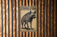 A sign with the text "STRIPPED HYENA" and an illustration of a striped hyena is displayed on a wooden wall.