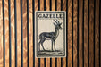 a sign with the name "Gazelle" on it, which is mounted on a wooden wall.