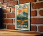 A vintage-style metal sign with a mountain landscape and a sun in the sky, mounted on a brick wall.