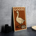 A vintage-style metal sign featuring a goose illustration and the text "GOOSE 60c" is displayed on a gray countertop.