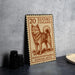 A wooden sign with a stamp design featuring a dog, placed on a table next to some black camera lenses.
