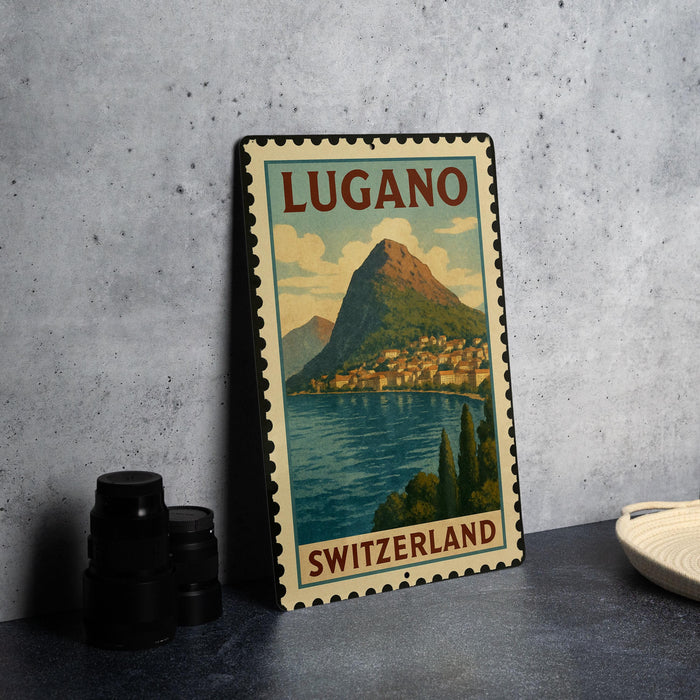A vintage-style metal sign depicting the town of Lucano, Switzerland, with a mountain in the background and a body of water in the foreground.