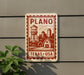 A sign for Plano, Texas, with a water tower and a barn in the background, mounted on a wall.