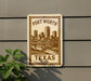A sign that reads "Fort Worth, Texas" with a cityscape illustration, mounted on a wall next to a plant.
