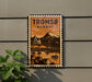 A vintage-style poster of the Tromsø-Norway bridge, featuring a mountain landscape and a small boat, is displayed on a wall.