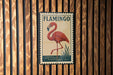 A vintage-style metal sign featuring a red flamingo standing on one leg in a pond, with the word "FLAMINGO" written above it.