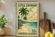 A framed vintage postage stamp depicting a tropical beach scene with palm trees and a sandy shoreline, placed on a shelf next to a wooden cutting board and a potted plant.