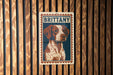 A metal sign with a picture of a dog, specifically a brittany dog, is displayed on a wooden wall.
