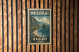 A vintage-style postage stamp from Hawaii, featuring a mountainous landscape with a beach and ocean, is displayed on a wooden wall.