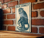 A metal sign featuring a blue monkey is mounted on a brick wall.