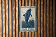 A blue and white sign with a picture of a pilot whale is mounted on a wooden wall.