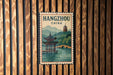 A vintage-style poster of Hangzhou, China, featuring a pagoda and a river, is displayed on a wooden wall.