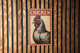 A vintage-style sign featuring a rooster is displayed on a wooden wall.