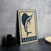 A metal sign with a blue and white design featuring a sailfish is displayed on a table.