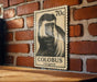 A vintage-style postage stamp featuring a close-up of a colobus monkey is displayed on a brick wall.