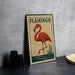 A vintage-style metal sign featuring a red flamingo standing on one leg in a pond, with a green border and the word "FLAMINGO" written in the top corner.