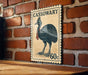 A vintage-style postage stamp featuring a large illustration of a black bird, likely a cassowary, mounted on a brick wall.