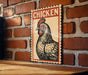 A vintage-style sign featuring a stylized illustration of a rooster is displayed on a brick wall.