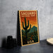 A vintage-style postage stamp featuring a desert landscape with cacti and mountains, along with the text "SAGUARO NATIONAL PARK USA".