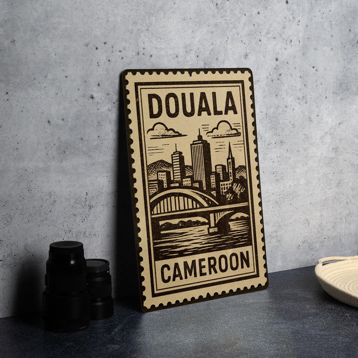 a stamp-like sign with the text "DOUALA CAMERON" and an illustration of a cityscape with a bridge.
