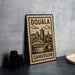 a stamp-like sign with the text "DOUALA CAMERON" and an illustration of a cityscape with a bridge.