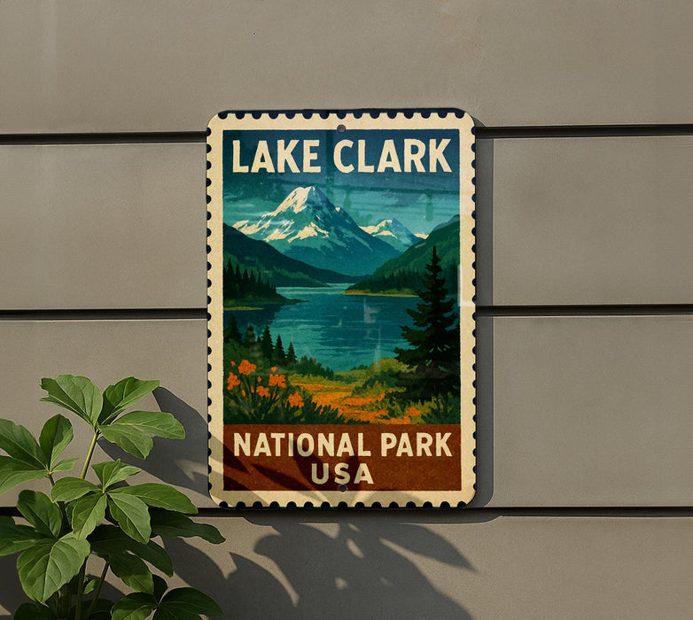 A vintage-style metal sign for Lake Clark National Park, featuring a scenic mountain landscape with a lake and pine trees.