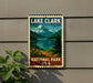 A vintage-style metal sign for Lake Clark National Park, featuring a scenic mountain landscape with a lake and pine trees.