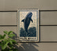 a sign with a blue and white illustration of a pilot whale, mounted on a wall.