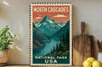 A vintage-style postage stamp depicting a scenic mountain landscape with a lake, surrounded by pine trees and mountains, is displayed on a wall next to a wooden cutting board and some potted plants.
