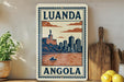 a decorative sign with the text "LUANDA ANGOLA" and an illustration of a cityscape with a boat on the water.
