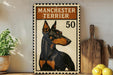 a framed poster of a Manchester Terrier dog, with the text "MANCHESTER TERRIER" and the number "50" printed on it. The poster is displayed on a shelf next to a wooden cutting board and a potted plant.