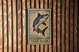 A metal sign with a tiger shark illustration is mounted on a wooden wall.