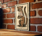 a wooden table with a framed illustration of a cat on it, mounted on a brick wall.