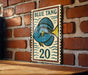A vintage-style sign featuring a blue fish with the text "BLUE TANG" and the number "20" on it, mounted on a brick wall.