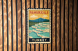 A vintage-style poster of Pamukkale, a famous geyser in Turkey, displayed on a wooden wall.