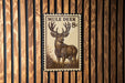 A wooden wall with a framed image of a mule deer, which appears to be a postage stamp or a decorative piece.