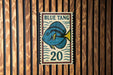 A vintage-style sign featuring a blue tang fish, with the number 20 below it, is displayed on a wooden wall.