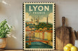 A vintage-style poster of Lyon, France, featuring a castle and a bridge, is displayed on a wall next to a wooden cutting board and some potted plants.