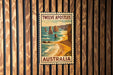 A vintage-style poster of the Twelve Apostles, a famous limestone formation in Australia, is displayed on a wooden wall.