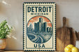A vintage-style metal sign with the text "Detroit Michigan USA" and an illustration of a city skyline, placed on a wooden surface next to a wooden cutting board and a potted plant.