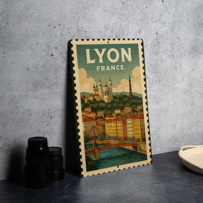 A vintage-style metal sign with the text "LYON FRANCE" and an illustration of a cityscape with a bridge, placed on a gray countertop next to some black camera lenses.