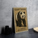 A framed poster of a panda bear is displayed on a table, with a stack of black camera lenses and a woven basket nearby.