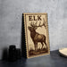 a wooden sign with a deer illustration, standing on a table next to some black camera lenses.